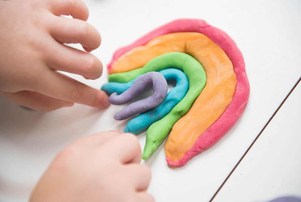 A child's hands making a rainbow out of playdough